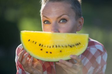 Güzel bir kadın yeşil arka planda sarı karpuz yiyor.