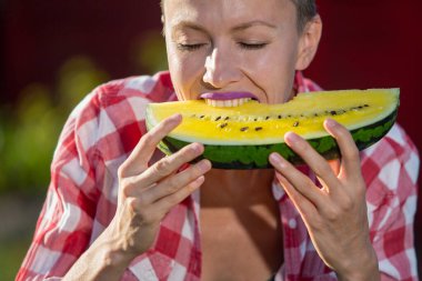 Güzel bir kadın yeşil arka planda sarı karpuz yiyor.