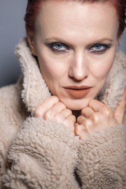 Gri arka planda yapay kürk giyen güzel kızıl saçlı kadın.