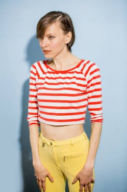 Kısa saçlı mutlu bir genç kadın, açık mavi arka planda doğal makyaj. Parlak kıyafetler giymiş güzel esmer bir kadının kapalı bir portresi. 