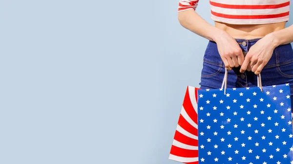 Beautiful woman holding shopping bags stars, stripes in white, blue, red colors  over light  blue background
