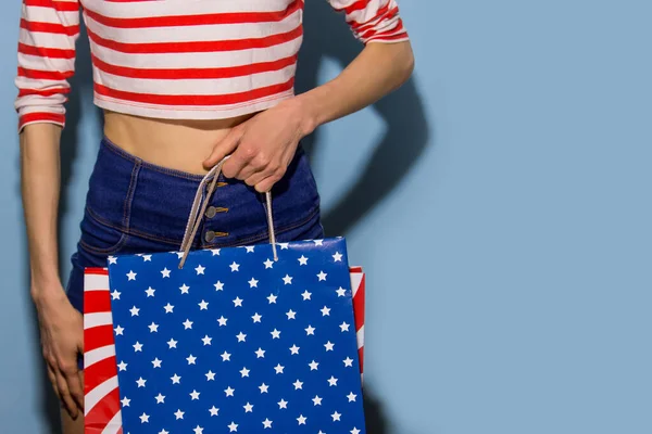 Happy shopping woman with shopping bags over blue background wearing striped clothing and shoping bags in patriotic colors