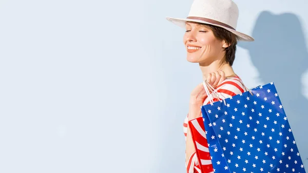 青の背景にストライプの服や愛国的な色のショッピングバッグを身に着けている上のショッピングバッグと幸せなショッピング女性 — ストック写真