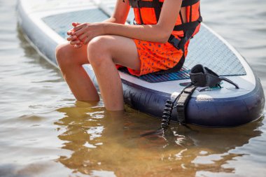 Boy sitting in a life jacket for water sport on . Boy or girl  wearing personal flotation device vest for sup study