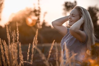 Uçan saçlı güzel bir kadın gün batımı ışığında yürüyor, tonlu bir görüntü.