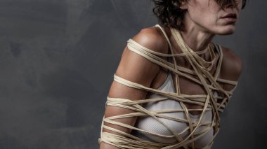 Gri duvarda iple sarılı bir kadının portresi.