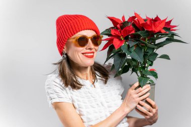 Kırmızı şapkalı kışın kırmızı çiçeklerini tutan neşeli güzel kadın. Noel buketi ile kışı hızlandıran kadın