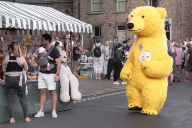Corbridge, Northumberland, Birleşik Krallık - 19 Haziran 2025: Corbridge şehir merkezinde yaz ortası kutlaması. Aile ayakta duruyor ve pazar meydanında bir oyuncak seçiyor.. 