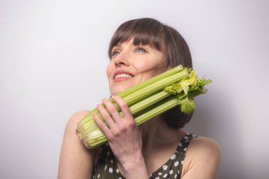 Gri arka planda kereviz tutan güzel bir kadın. Sağlıklı beslenme, diyet, kilo kaybı, detoks kavramı