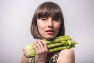 Bayan Kereviz. Gri arka planda kereviz tutan güzel bir kadın. Sağlıklı beslenme, diyet, kilo kaybı, detoks kavramı