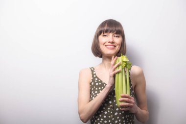 Bayan Kereviz. Gri arka planda kereviz tutan güzel bir kadın. Sağlıklı beslenme, diyet, kilo kaybı, detoks kavramı