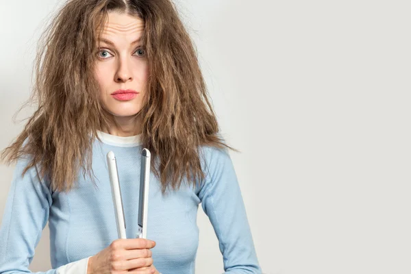 Funny woman with messy hair holding straightening irons — Stock Photo, Image