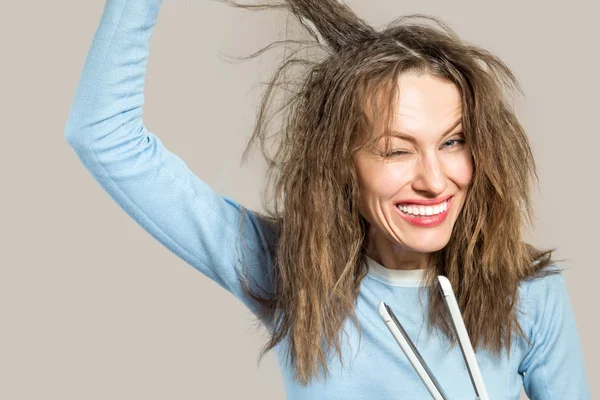 Забавная женщина с грязными волосами, держащая выпрямляющие утюги — стоковое фото