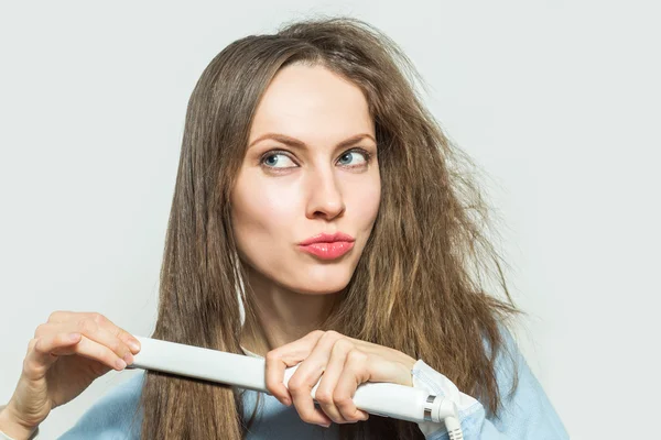 Mujer divertida con cabello desordenado sosteniendo planchas de alisado — Foto de Stock