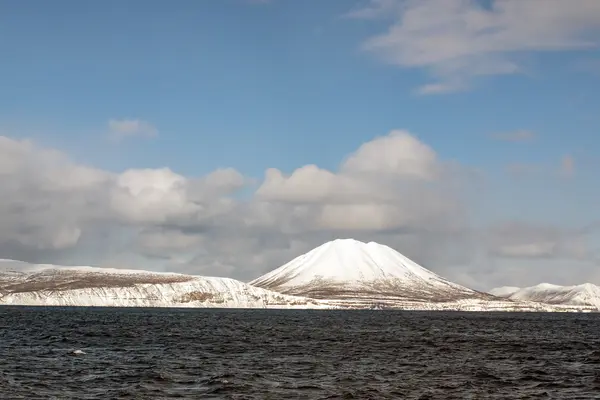 Снежный вулкан на фоне моря и голубого неба — стоковое фото