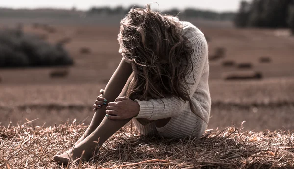 Retrato de larga duración de niña adulta joven cerca de pajar contra el cielo azul con nubes y campo de otoño triste Fotos de stock libres de derechos