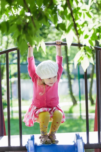 Tres años de edad, niña jugando en el patio de diapositivas y colgando en el travesaño — Foto de Stock