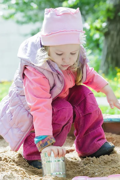 Three years old girl playing with metal tin can in playground sandbox — Stock Photo, Image