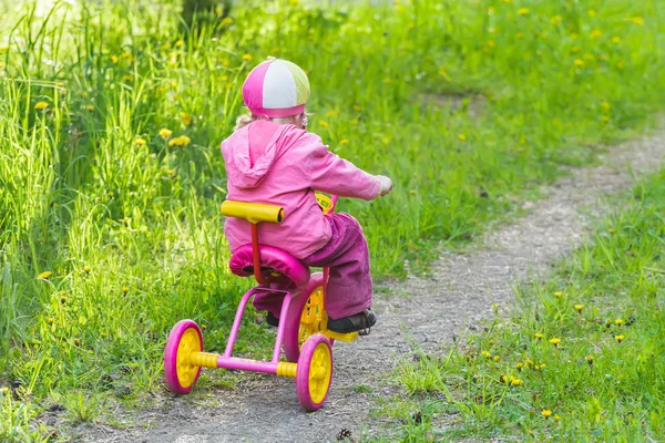 小女孩孩子粉色和黄色三轮车骑公园轨道的背影全长肖像 — 图库照片
