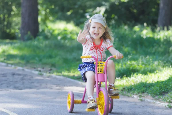 Dwa-letni roześmiany dziewczyna noszenia sztruks płaską czapkę i polka-dotted kostium na rowerze dzieci trójkołowy różowy i żółty — Zdjęcie stockowe