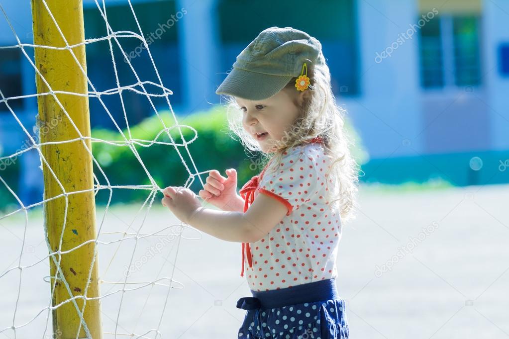 Nursery school girl playing near football goal net with yellow goalposts