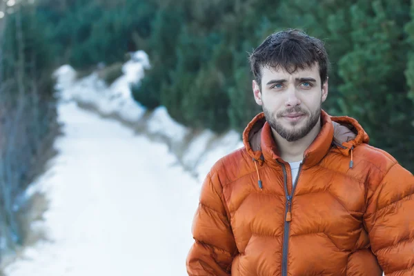 Outdoor portrait of young handsome man wearing beard and orange winter down jacket — Stock Photo, Image