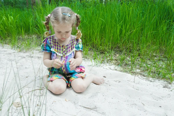 Маленькая девочка играет на пляжной дюне и рассматривает маленький желтый лист в руке — стоковое фото
