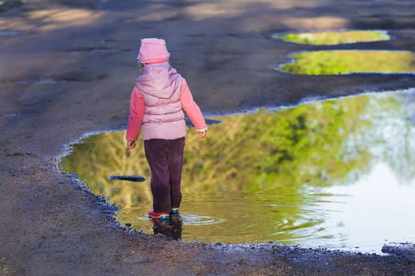 Pohled zezadu na procházky v jarní louže preschooler dívka na sobě fialové nylon a růžová lopaty klobouk — Stock fotografie