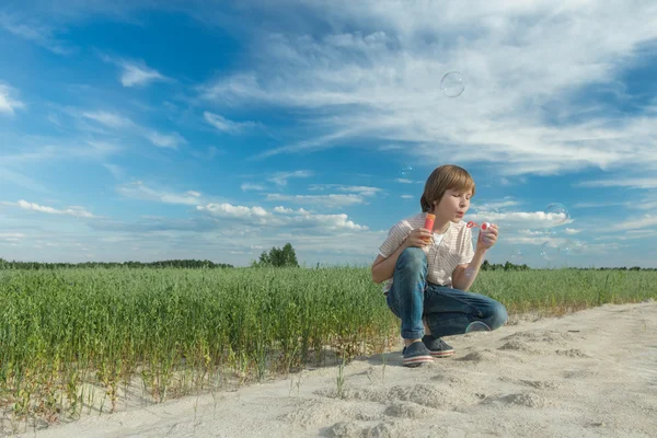 Kavkazská teenager foukání mýdlová bublina hůlka pro výrobu mýdlové bubliny na nezpevněnou ovesné oblasti — Stock fotografie