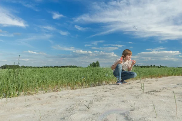 Tonårspojke blåser såpbubbla trollspö för att göra såpbubblor på grusväg gård fältet — Stockfoto