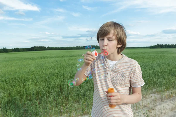 Portrét chlapce, teenagera kavkazského s plovoucí mýdlové bubliny na prašné polní hospodářství polní cesty — Stock fotografie