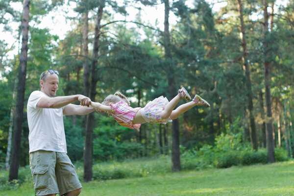 Happy father spinning around his daughter in green summer park outdoors