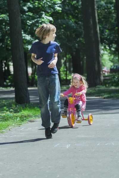 Rire soeur fratrie courir après son frère sur rose et jaune enfants tricycle — Photo