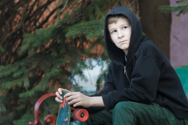 Ritratto di adolescente a riposo che tiene lo skateboard e si siede sulla panchina del parco — Foto Stock