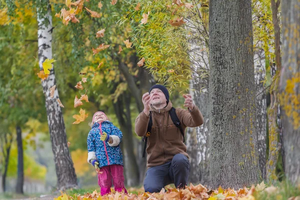 Padre sorridente con figlia ridente che lancia foglie gialle autunnali nel parco all'aperto — Foto Stock