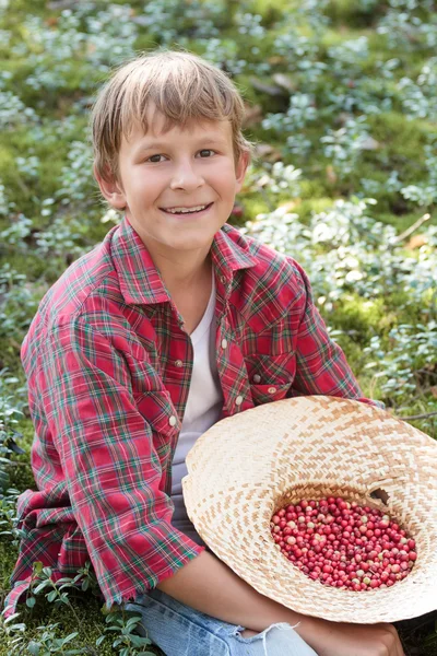 Leende pojke håller hatten full av röda wildberries — Stockfoto