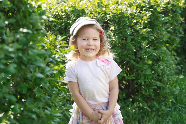 Twee-jarige lachen meisje in corduroy platte GLB bij groene tuin struikgewas achtergrond — Stockfoto