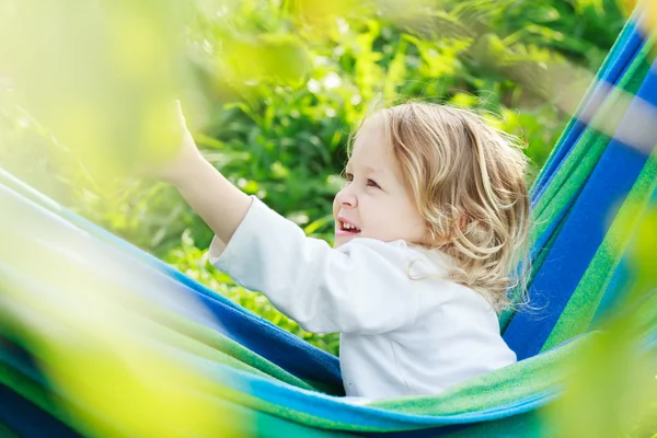 Two year-old toddler girl is laughing and playing in striped blue-green Brazilian hammock — Stock Photo, Image