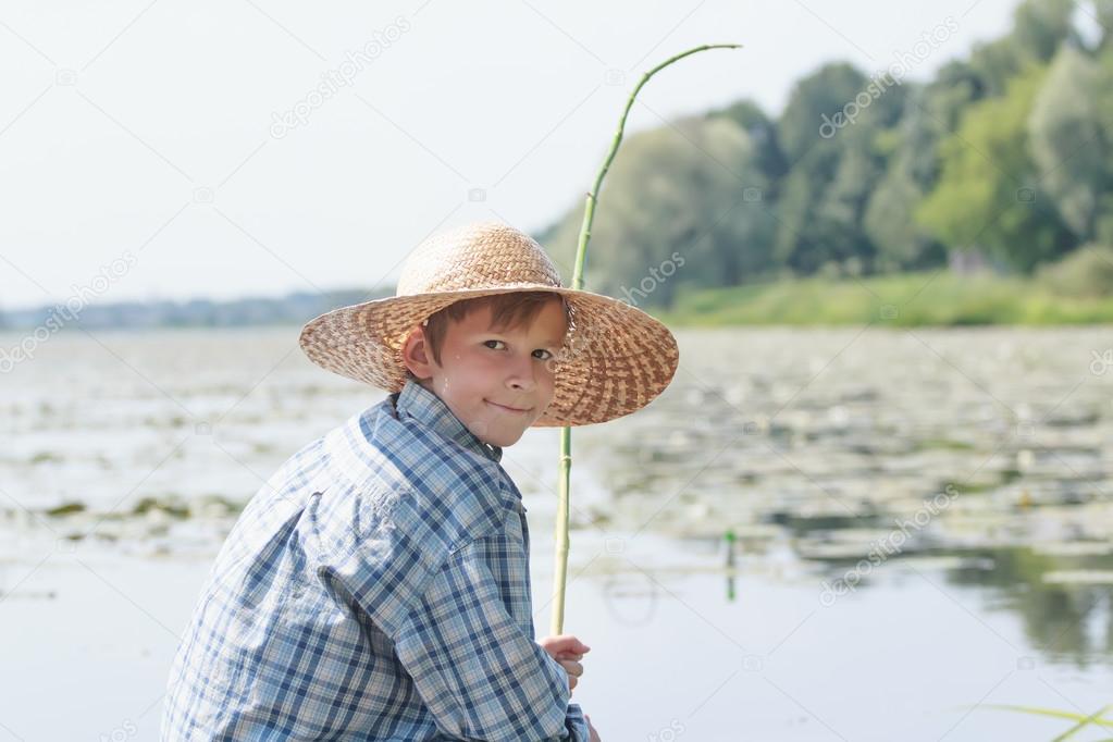 Angling teenage boy with handmade green twig fishing rod is looking back