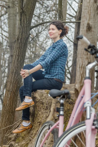 Attraente bruna ragazza seduta su enorme vecchio albero ceppo con rosa vintage bici in primo piano — Foto Stock