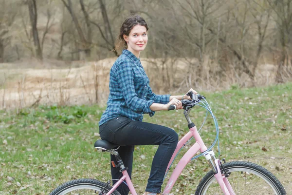 Allegro ragazza bruna in bicicletta su pista sterrata nel vecchio parco — Foto Stock