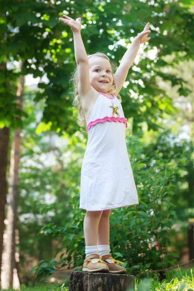 Blond meisje permanent met opgeheven handen op boom stomp volledige lengte — Stockfoto