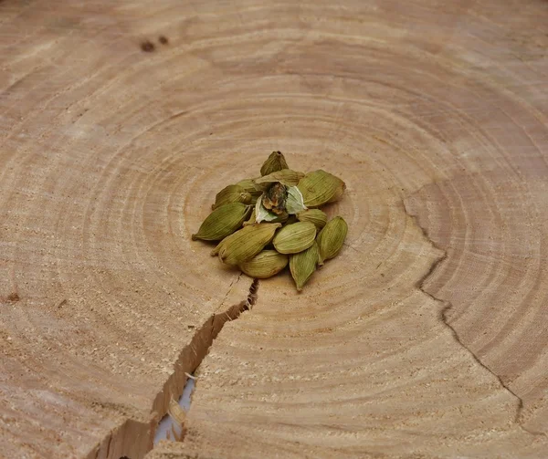 Eine Handvoll grüner Kardamom auf einem quer geschnittenen Baum — Stockfoto