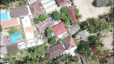 Rotasyon uçuşu. Nusa Penida, Endonezya 'daki tropik bir adada palmiyelerin arasına gizlenmiş kırmızı çatı bungalovları. Rotary uçuş. Döndürme. Döndürme