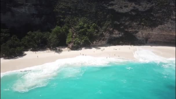 Widok z lotu ptaka na turystów na Kelingking Beach cieszących się falami na ich ciałach. Niezidentyfikowani ludzie na plaży Kelingking. Ogromne fale zagrażają turystom na plaży. Filmik z powietrza 4K — Wideo stockowe