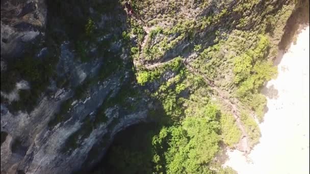 Turisté kráčejí po strmé stezce ke Kelingkingské pláži, Nusa Penida. U útesu na pláži se shromažďují neidentifikovatelní lidé. Turisté jdou po schodech na Kelingkingskou pláž. Letecké 4K video — Stock video