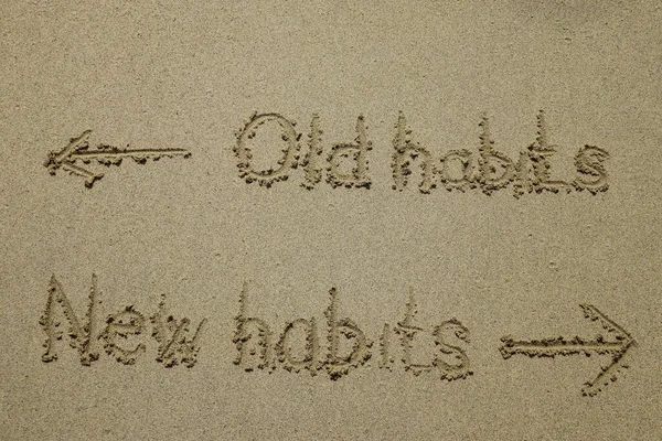 old habits vs new habits, life change concept written on sand.