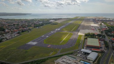 Ngurah Rai Uluslararası Havalimanı 'ndan kalkan uçağın Bali Adası manzarası. Okyanusa uzanan pist. Denpasar 'daki uluslararası havaalanına hava görüntüsü