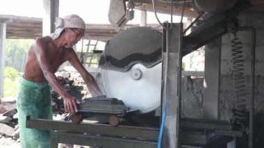 Denpasar, Bali, Endonezya, 12 Ağustos 2020. Asyalı bir adam dairesel testere ile bir taş keser. Asyalı erkeklerin portresi siyah volkanik taşı ikiye bölmek için elektrikli testereler kullanıyor..