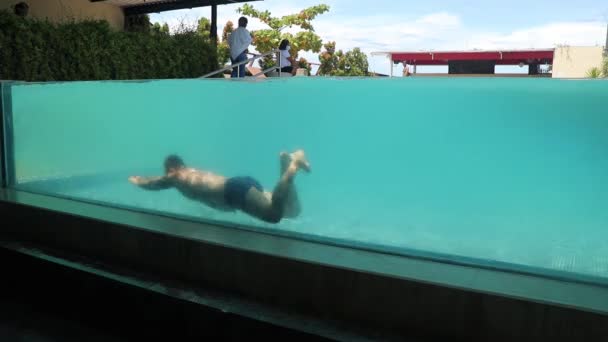 Kuta, Bali, Indonesia, 14 de marzo de 2021. Foto submarina del hombre caucásico buceando en la piscina con pared de cristal transparente en el hotel Atanaya. borde de la piscina infinito de lujo — Vídeos de Stock